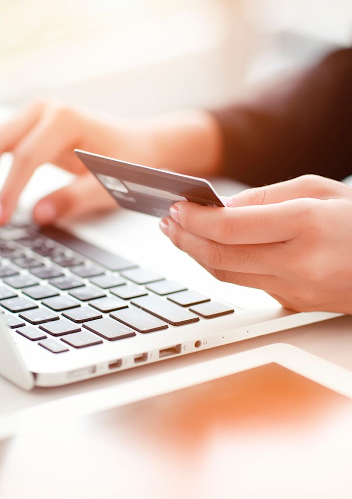 En hand håller ett kreditkort och skriver på en bärbar dator i en ljus miljö.