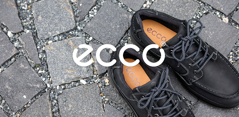 Svarte ECCO skinnsko i casual stil med reflekterende lisser plassert på brosteinsunderlag, med ECCO-logo synlig.