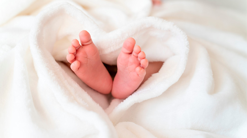 Nyfödda bebisfötter som sticker ut från en mjuk, vit filt formad som ett hjärta.