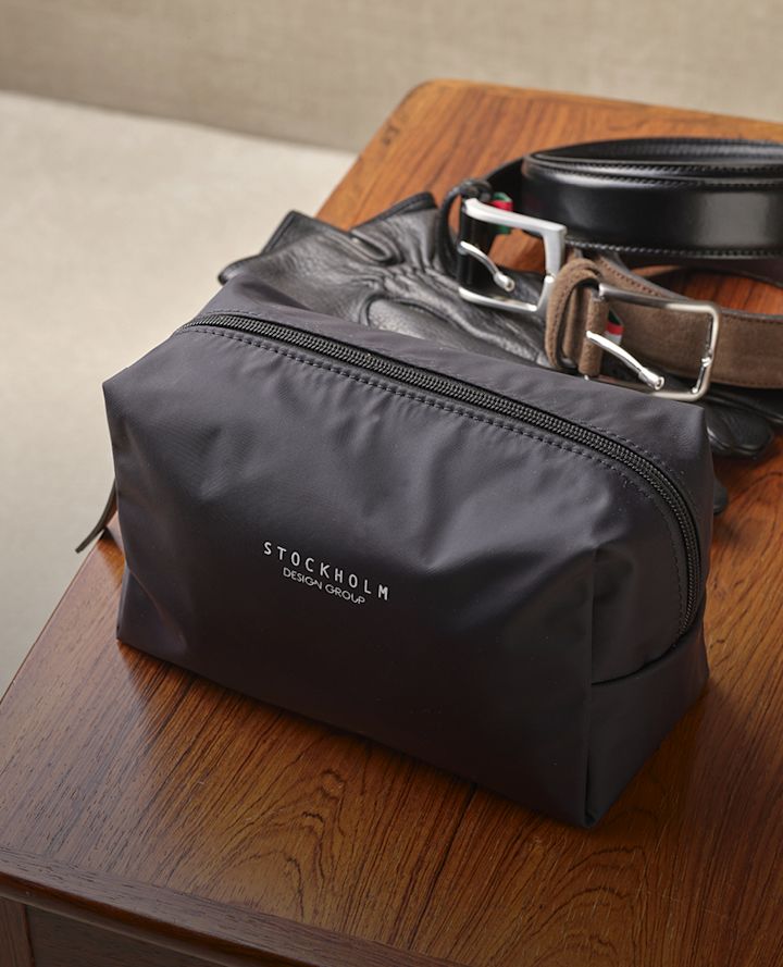 Svart toalettmappe fra Stockholm Design Group på trebord med svart og brun lærbelter ved siden av.