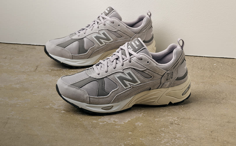 Grå New Balance løpesko med mesh og semsket skinn, tykk beige såle og svart yttersåle, plassert på betonggulv.